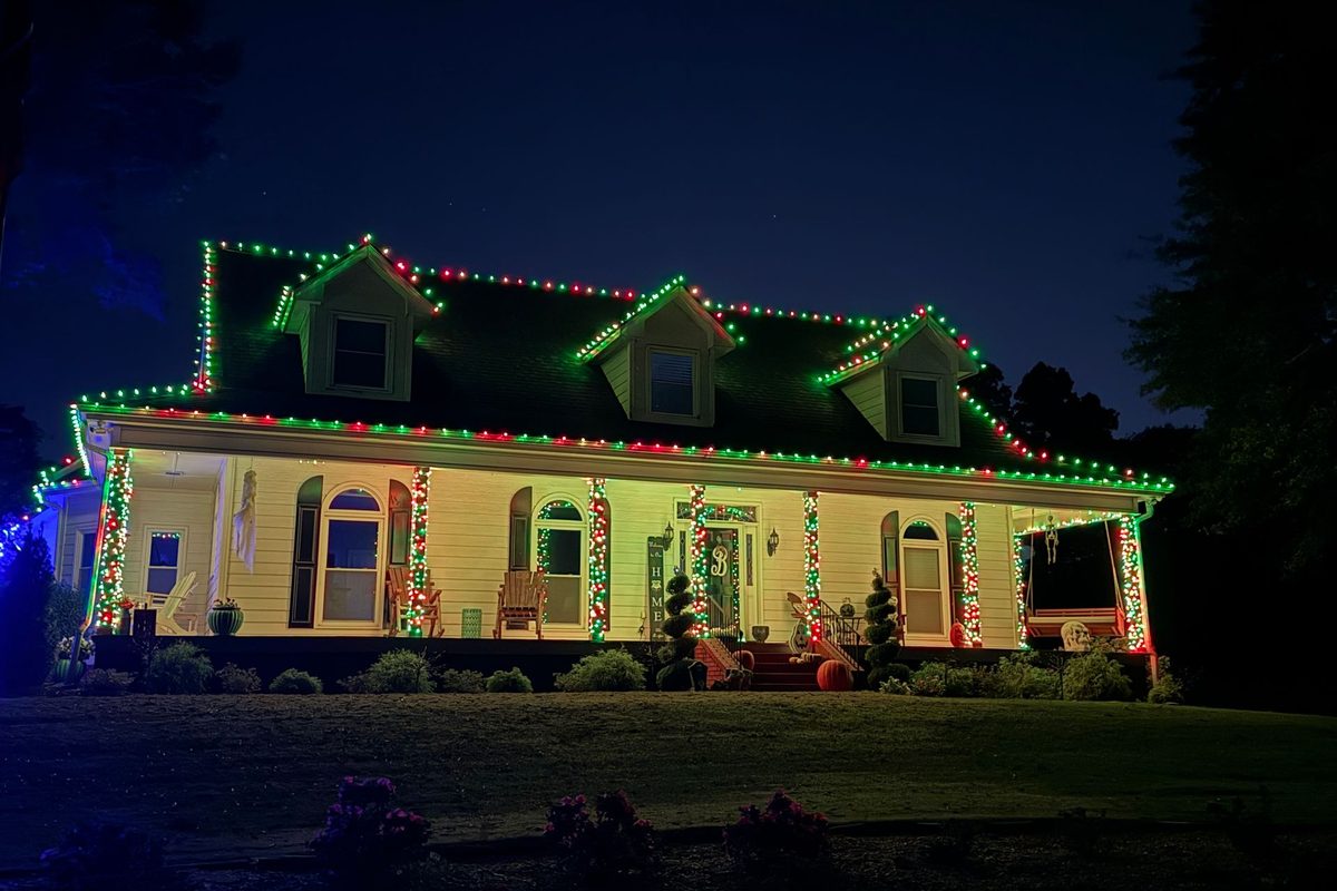 Red and green holiday lighting along a roofline, porch columns and dormers